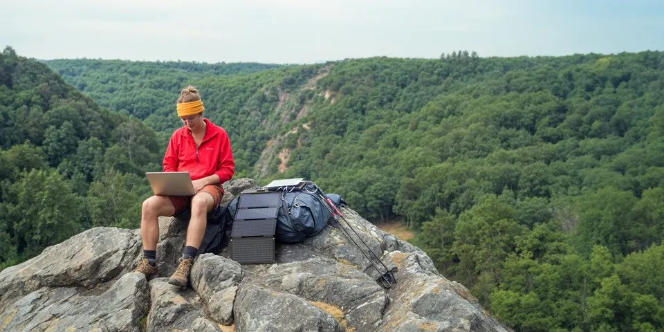 SORA 60 encostado na mochila, no alto de uma pedra, carregando um tablet pelo USB